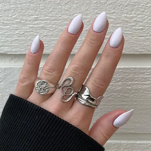En kvinnohand med ringar och vackra korta naglar med vitt nagellack med lila undertoner