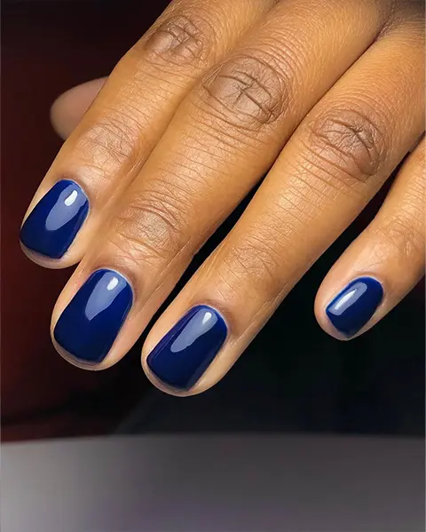 En hand med mörkblått skimrande nagellack